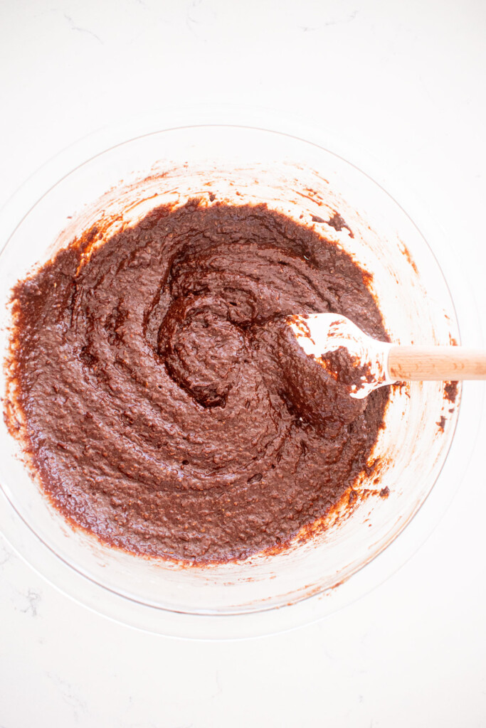 chocolate cake batter in a glass mixing bowl with a spatula on a white marble counter.