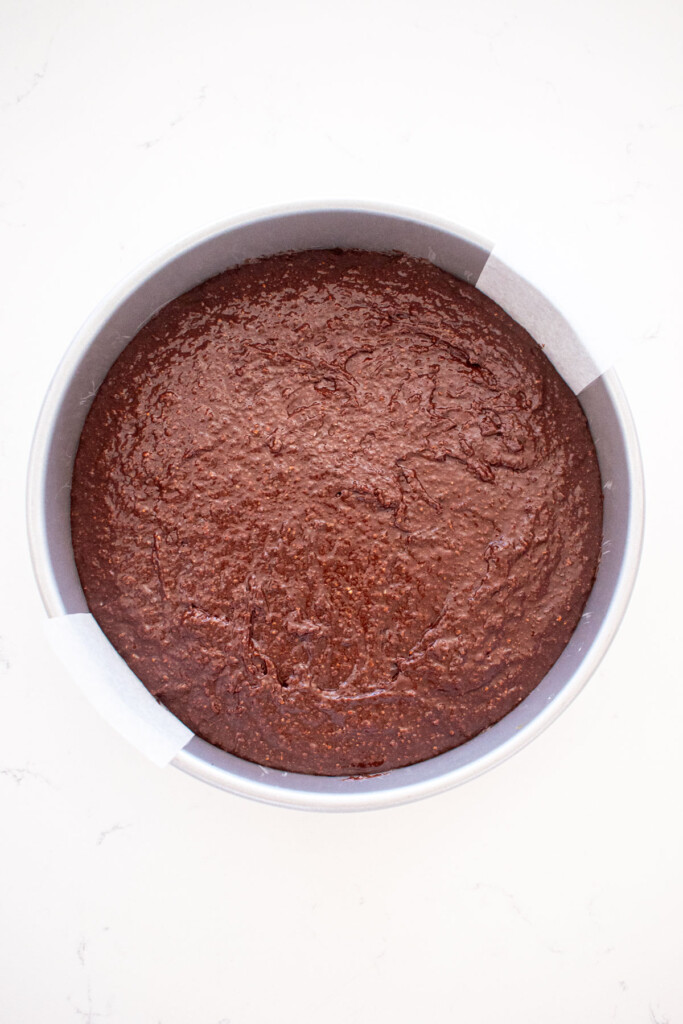 chocolate cake batter in a cake pan on a white marble counter.