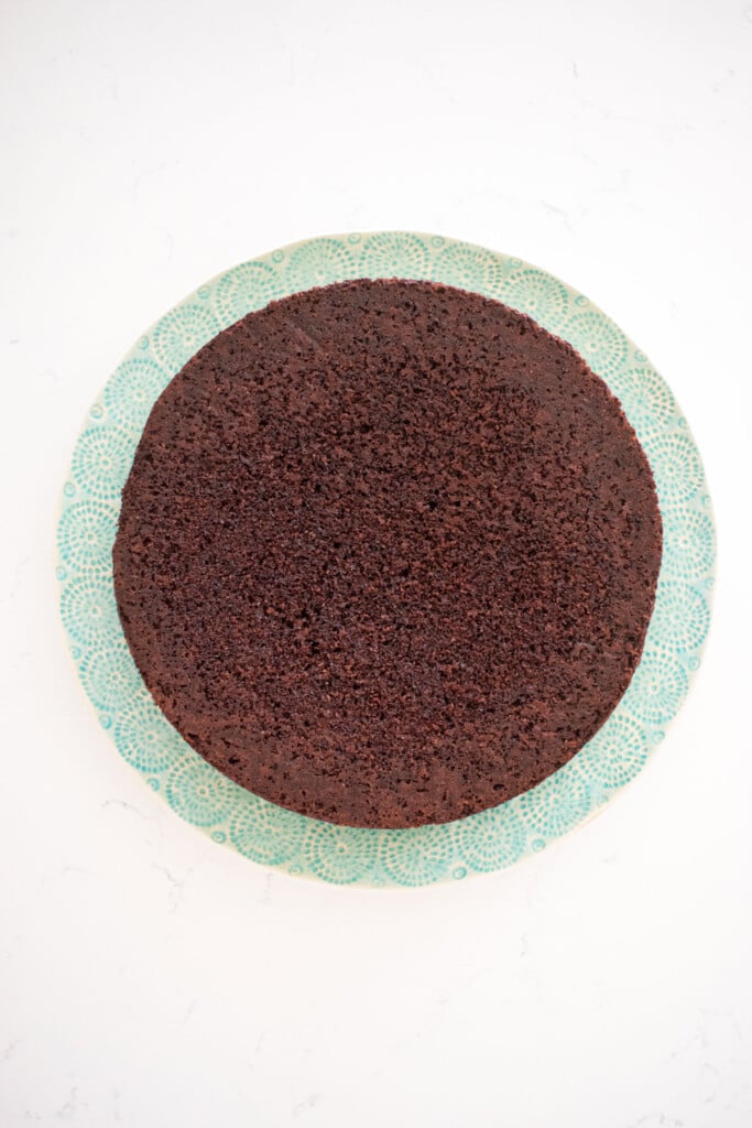chocolate cake on a green cake plate on a white marble counter.