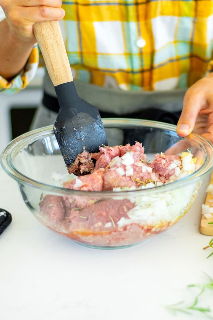 woman stirring rosemary meatball ingredients together in a glass mixing bowl.