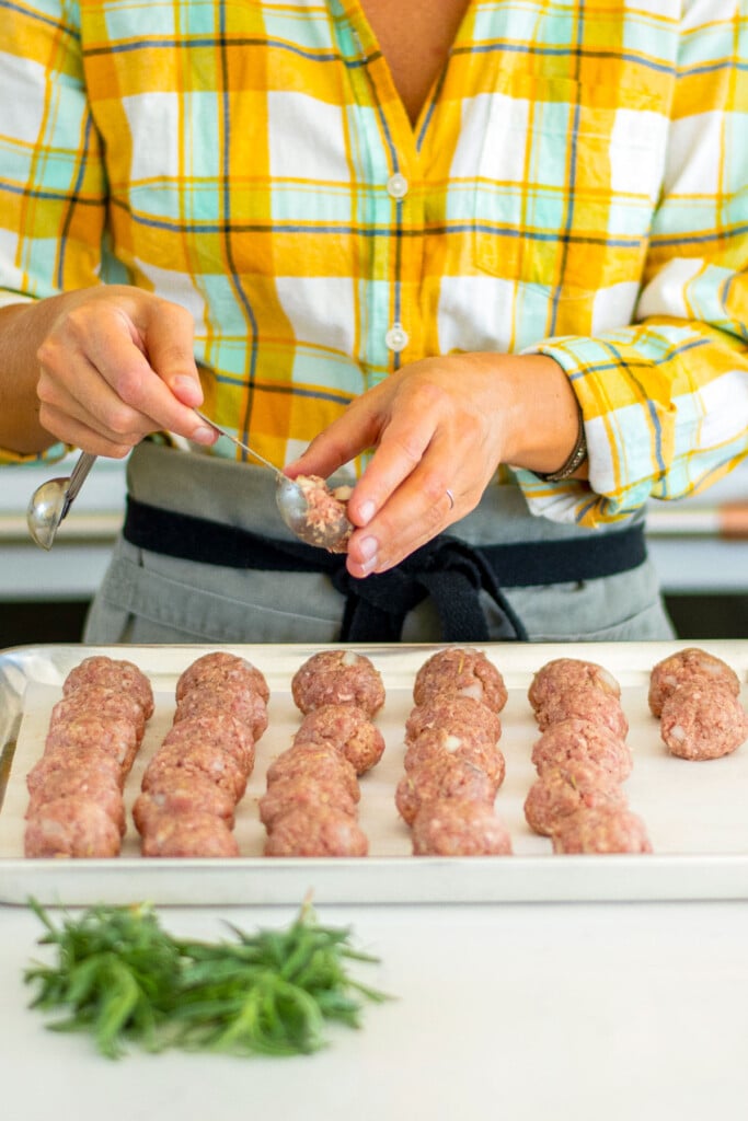 woman forming rosemary meatball bites with a tablespoon and placing on a baking sheet.