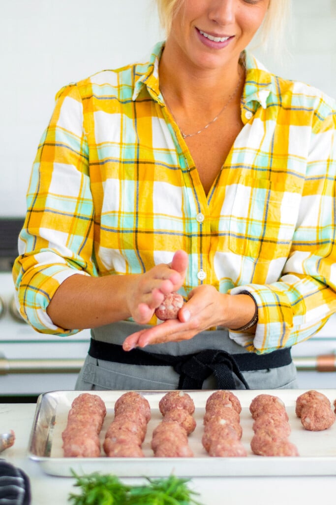 woman rolling meatballs with her hands standing at the kitchen counter.