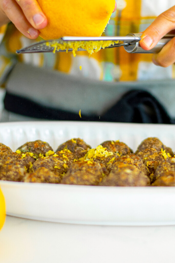 woman grating lemon zest on top of rosemary meatball bites.