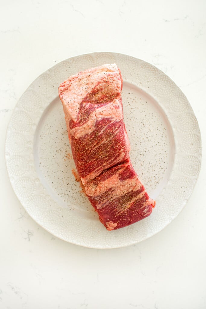 beef brisket on a plate with salt and pepper on a white marble counter.