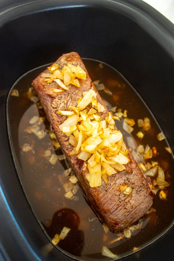 seared brisket in a slow cooker with sauted onions and bone broth.
