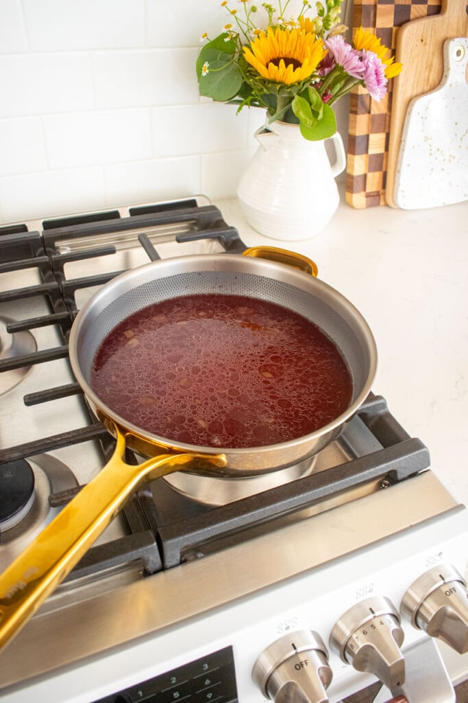 large skillet with beef broth and red wine on a stovetop.