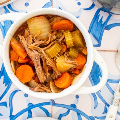 mini dutch oven with slow cooker beef brisket stew on a blue tile table with a glass of red wine.