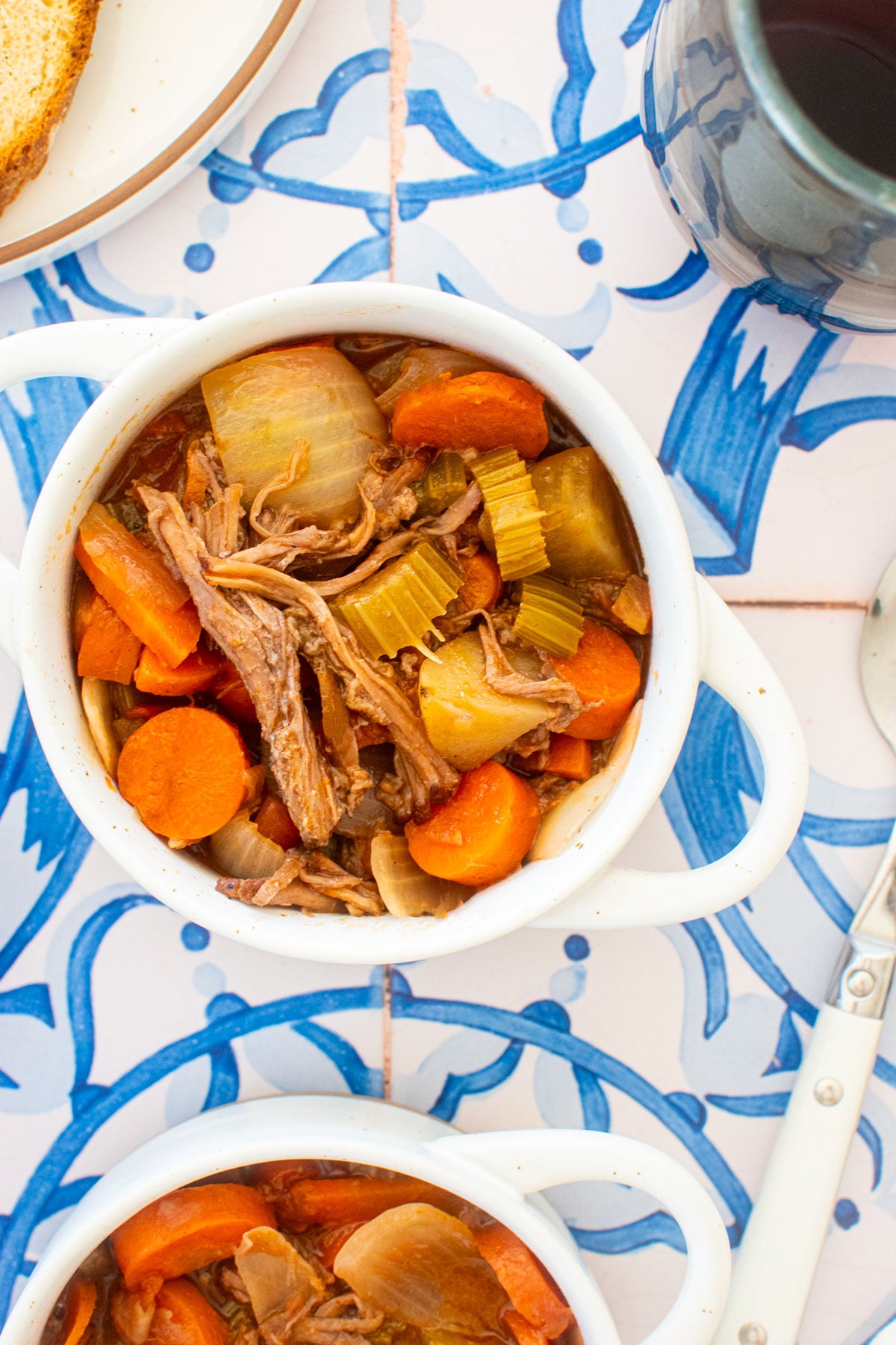 mini dutch oven with slow cooker beef brisket stew on a blue tile table with a glass of red wine.