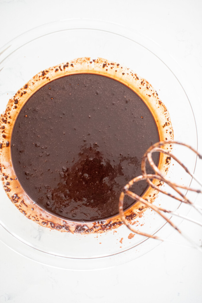 wet ingredients for vegan brownies mixed together in a glass mixing bowl on a white marble counterl.