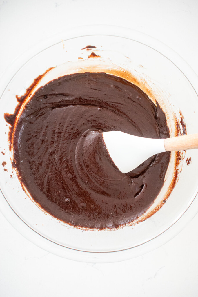 vegan brownie batter in a glass mixing bowl on a white marble counter.