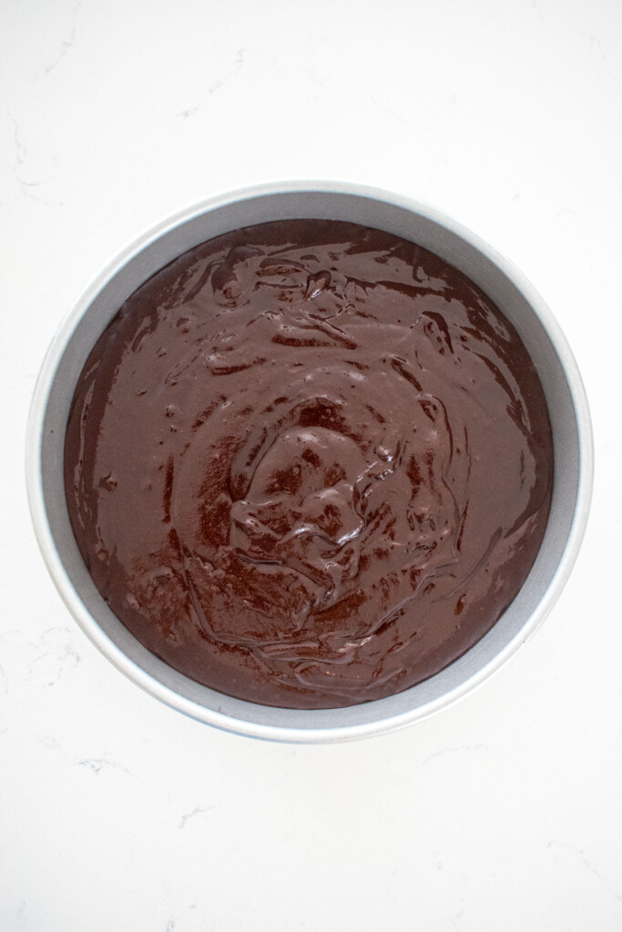 vegan brownies in a round cake pan on a white marble counter.