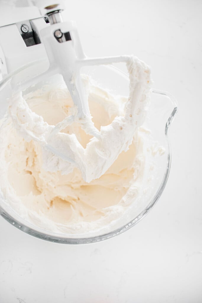vegan frosting in a glass mixing bowl on a white marble counter.