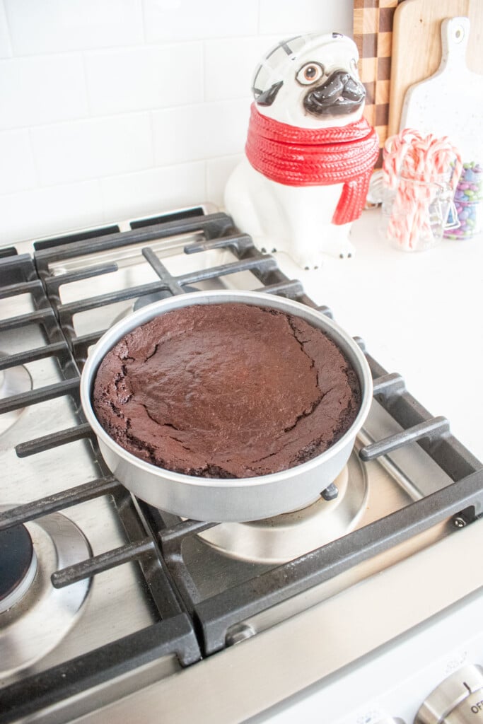 baked vegan brownies in a round cake pan on top of an oven cooling.