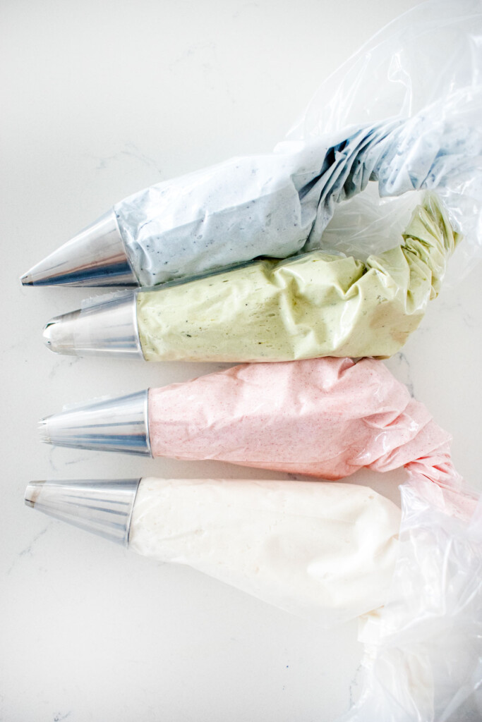 four piping bags with light blue, green, pink and white frosting on a white marble counter.
