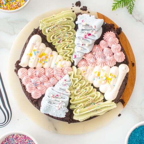 vegan christmas tree brownies frosted with different colors on a serving board on a marble counter with bowls of sprinkles.