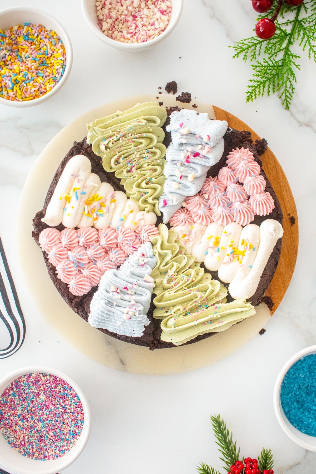 vegan christmas tree brownies frosted with different colors on a serving board on a marble counter with bowls of sprinkles.