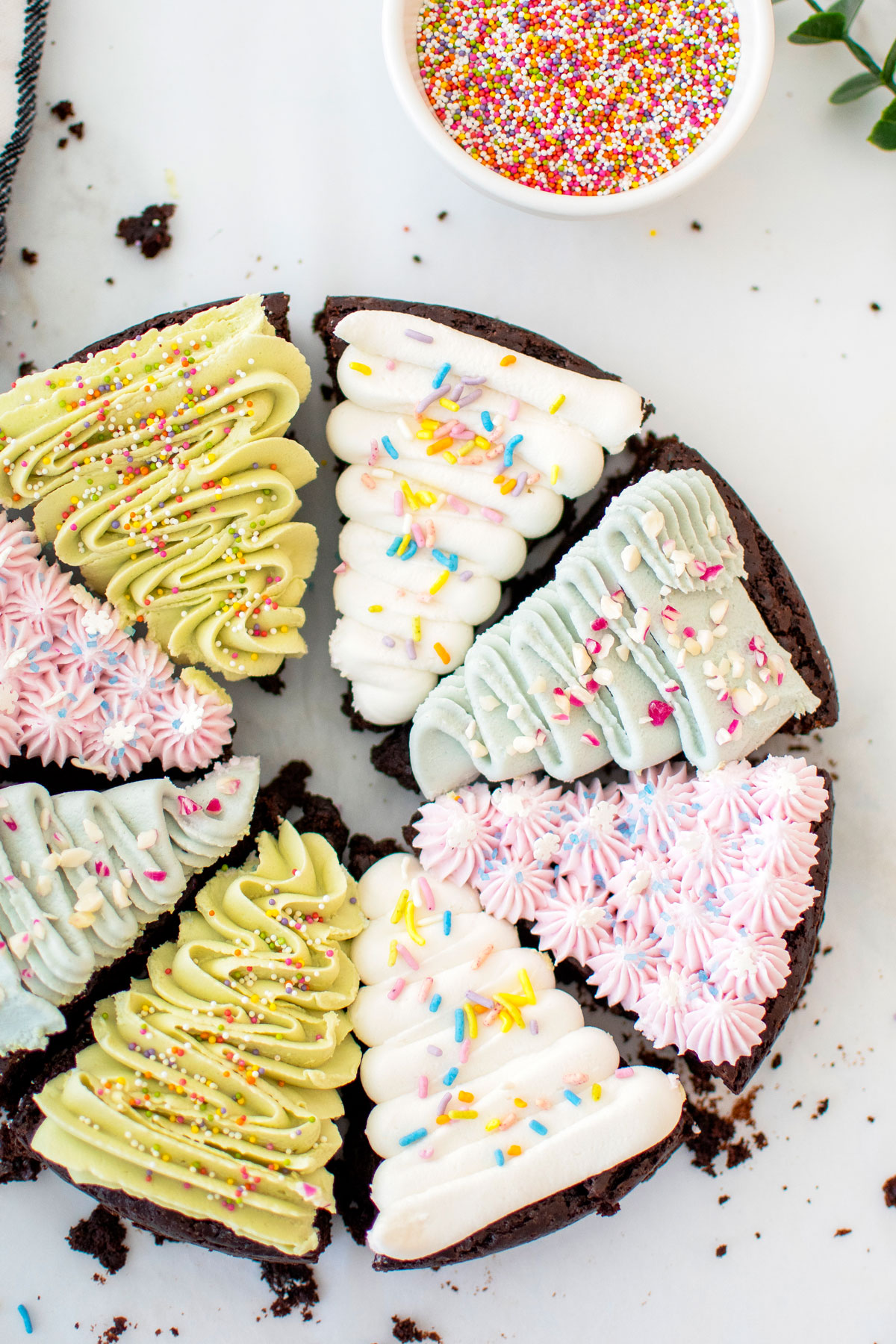 vegan christmas tree brownies decorated with different colored frosting and sprinkles on a white marble counter.