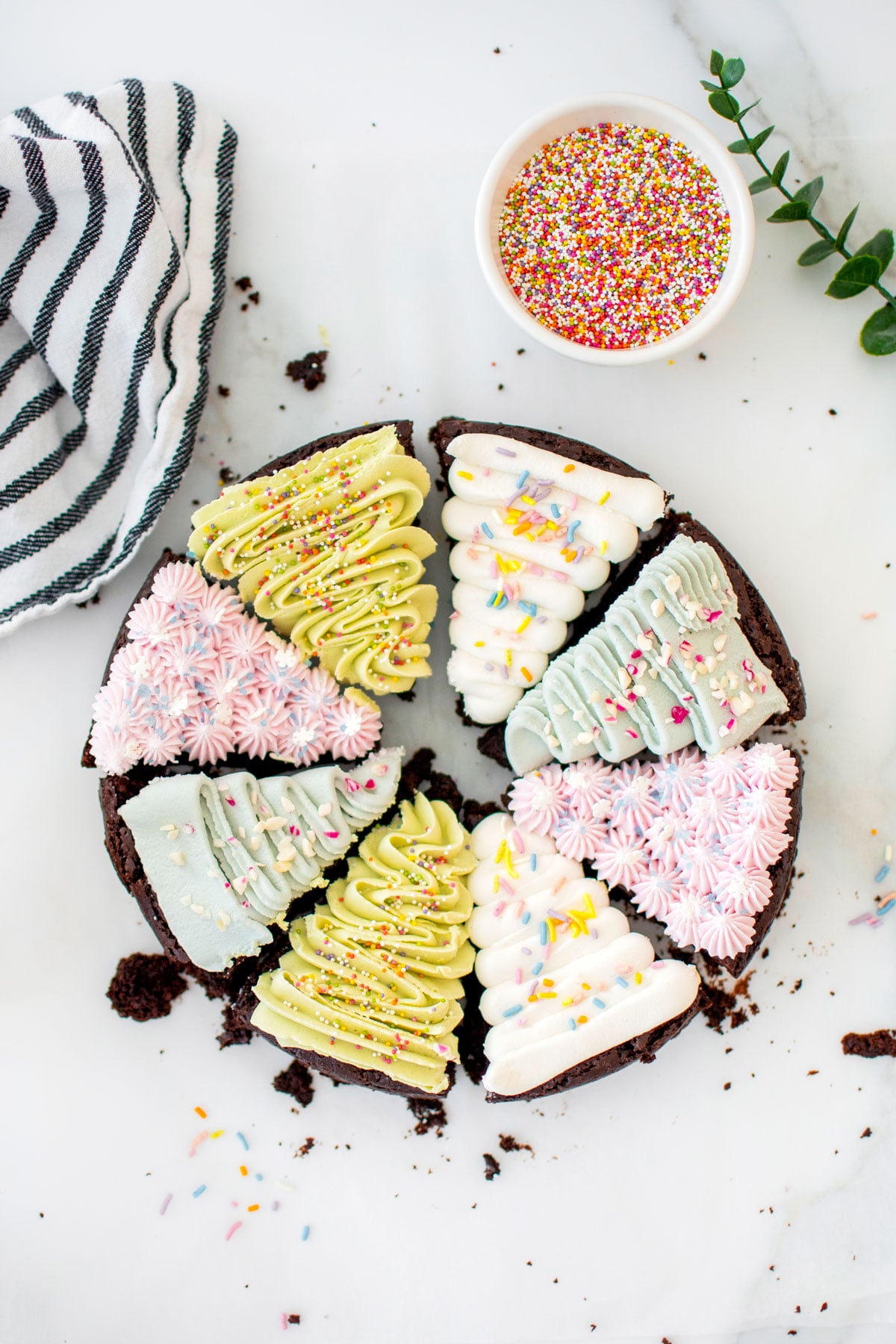 vegan christmas tree brownies decorated with different colored frosting and sprinkles on a white marble counter.