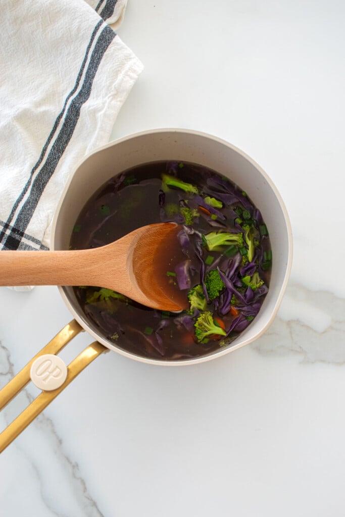 bone broth vegetable soup in a small pot with a wooden spoon on a marble counter.