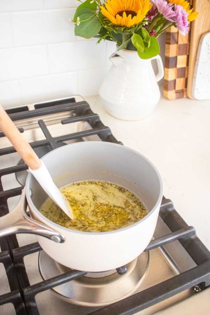 small saucepan with melted butter and herbs on a stovetop.