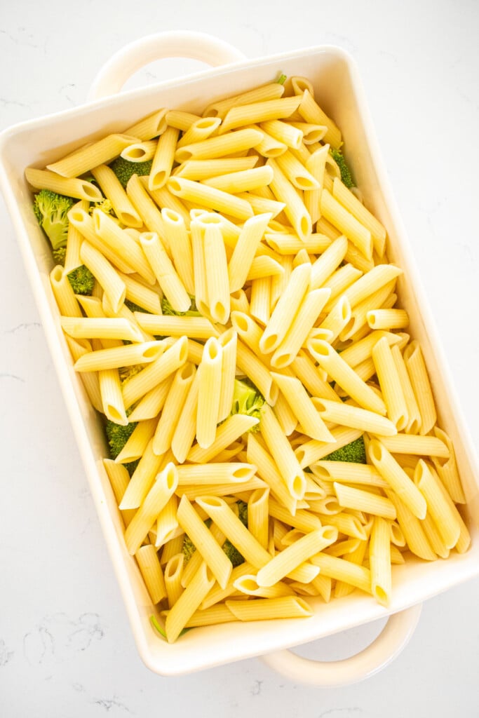 baking dish on a white marble counter with broccoli, spinach and penne pasta.
