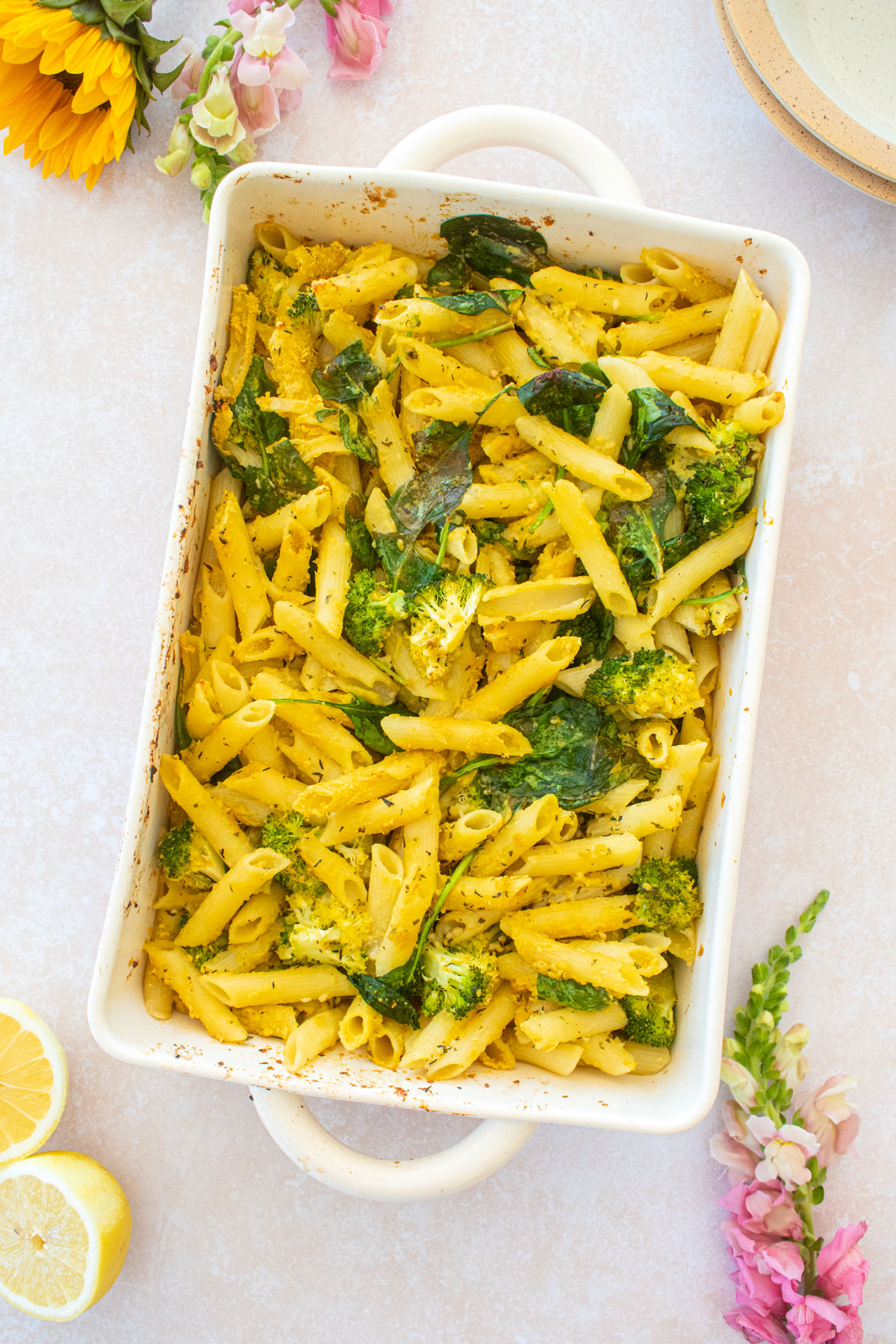 baked butter lemon pasta in a hot dish on a table with fresh flowers, lemons, and bowls.