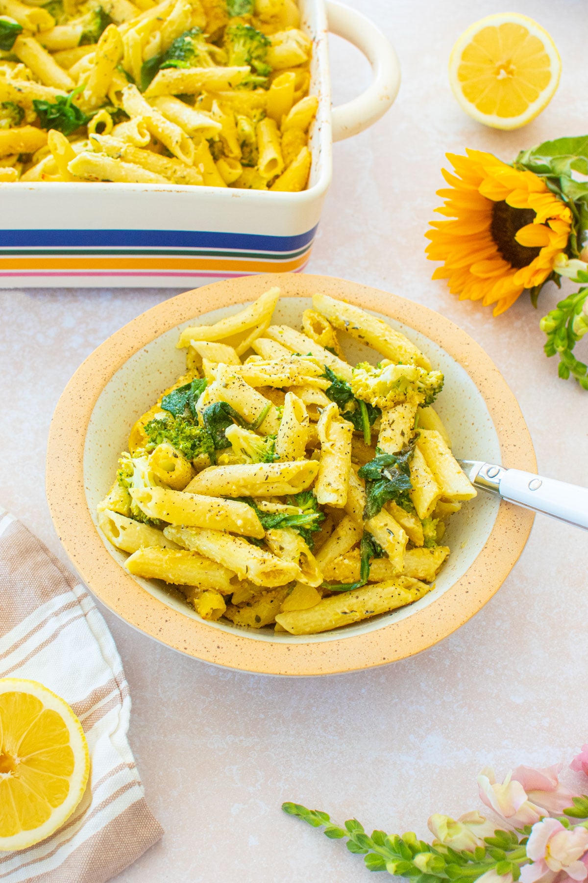bowl of baked butter lemon pasta without cheese in a pasta bowl on a table with fresh flowers and lemons.