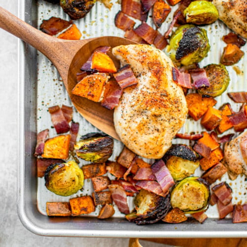 cooked chicken breast on a sheet pan with charred brussels sprouts, sweet potato and bacon bits.