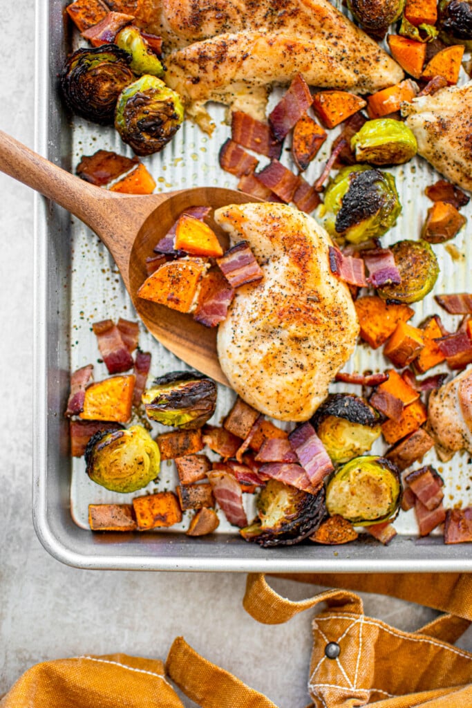 cooked chicken breast on a sheet pan with charred brussels sprouts, sweet potato and bacon bits.