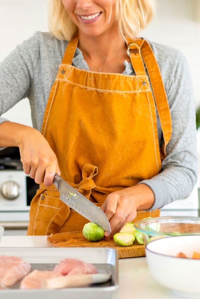 woman cutting brussels sprouts on a wood cutting board in the kitchen.