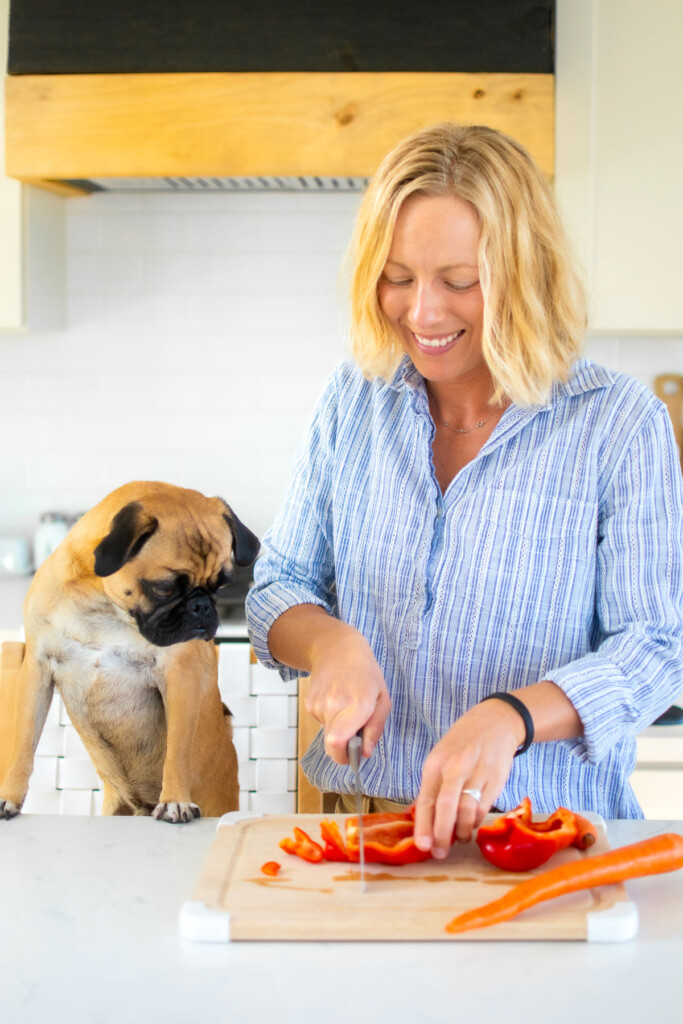 woman and pug in kitchen cutting up carrots and bell peppers.