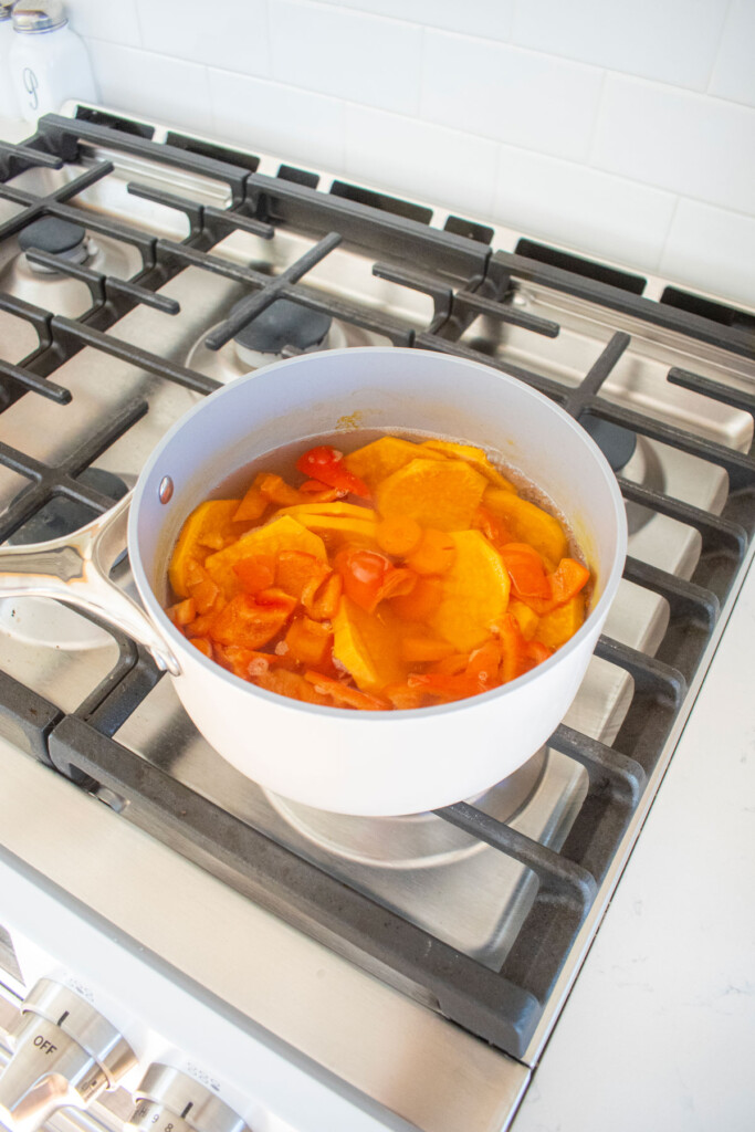 carrots, bell peppers and sweet potatoes coking in a bot over the stovetop.