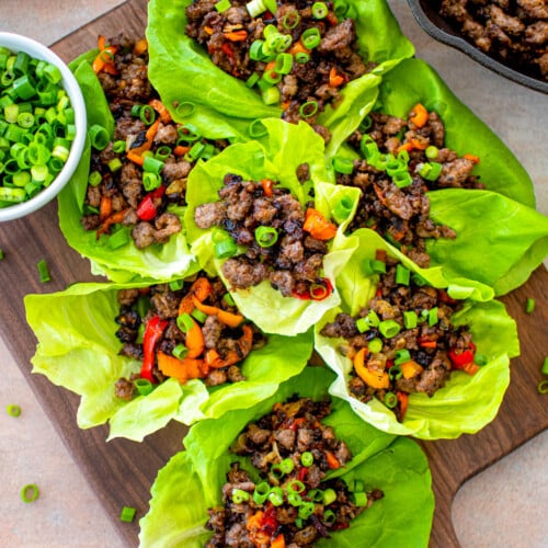 chinese five spice lettuce cups with pork on a wood serving board with a small bowl of green onions.
