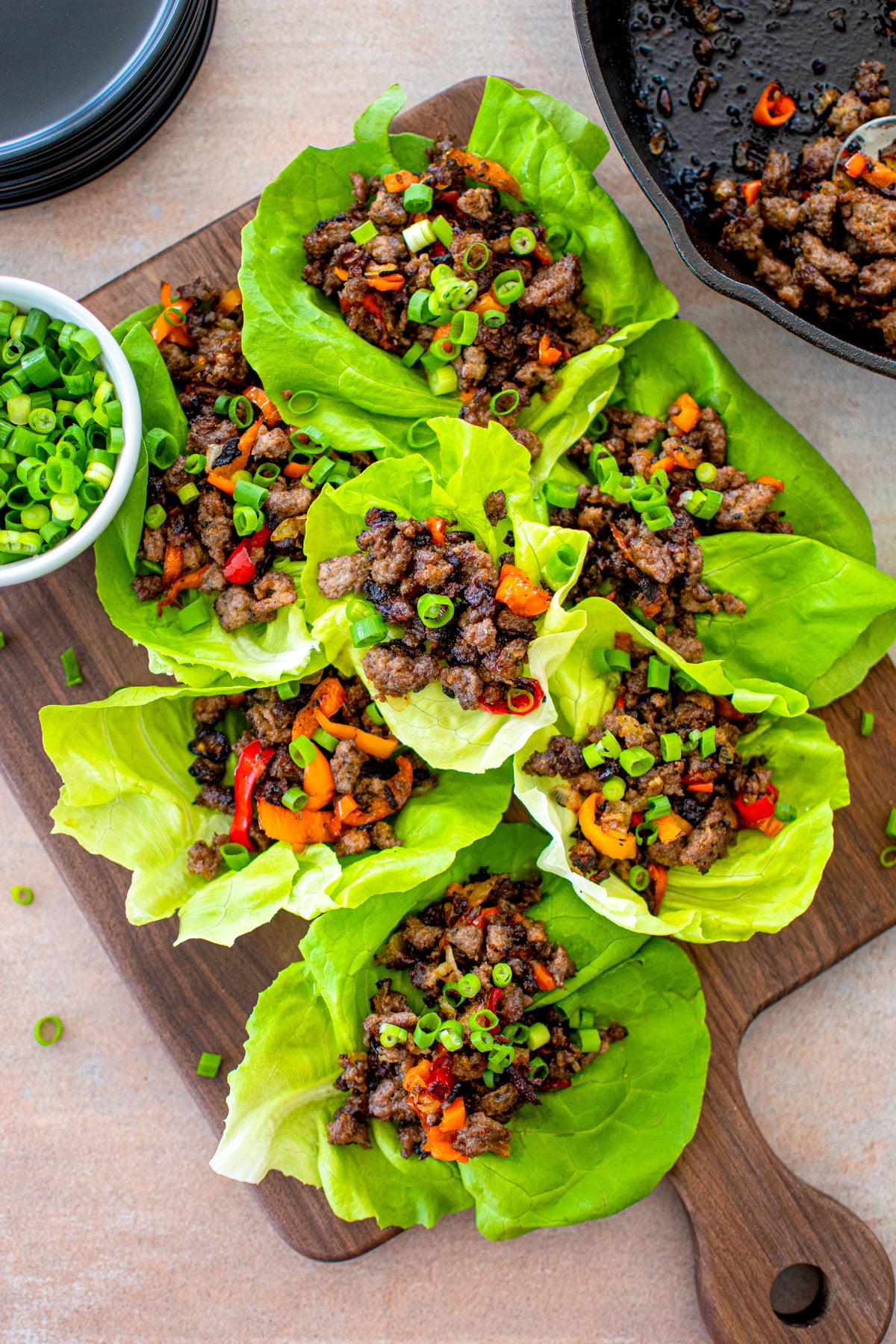 chinese five spice lettuce cups with pork on a wood serving board with a small bowl of green onions.