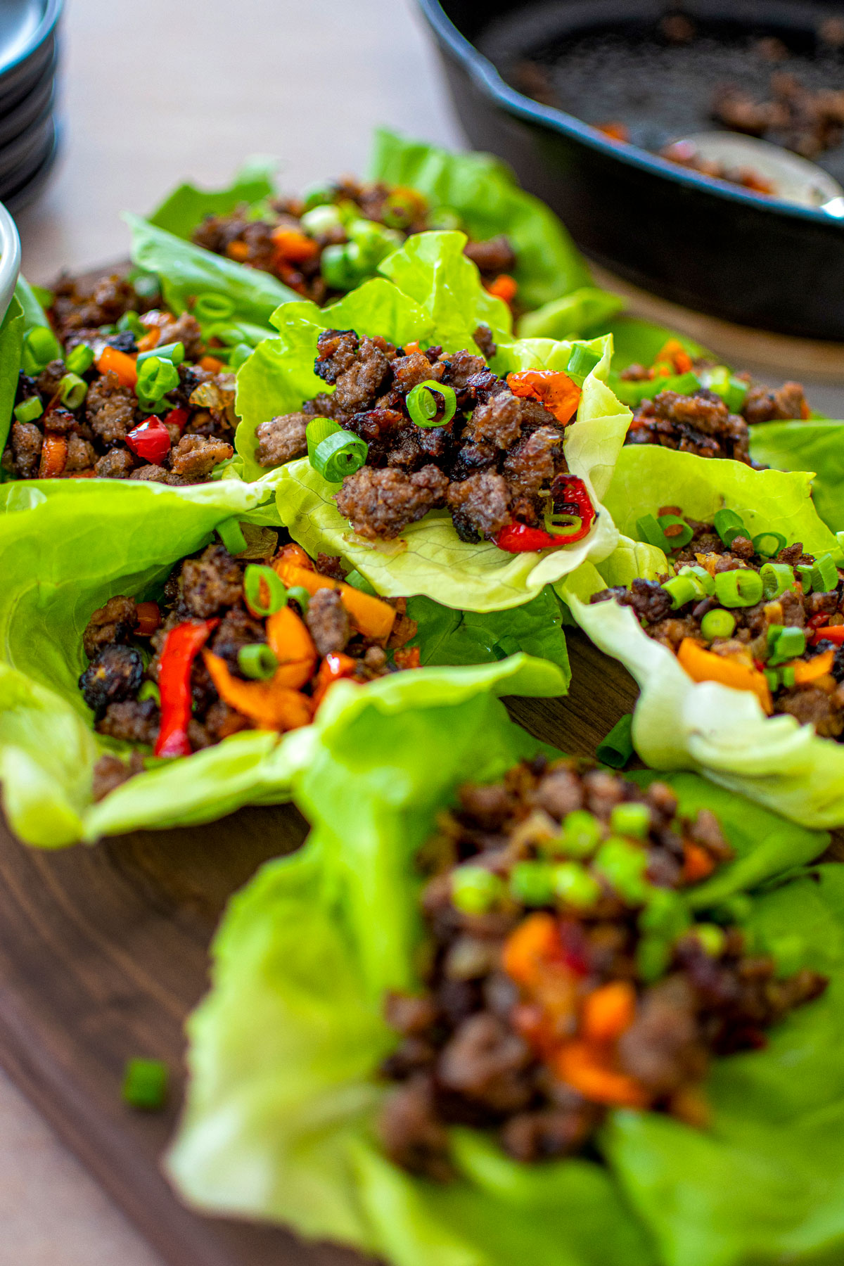 chinese five spice lettuce cups with pork on a wood serving board with a small bowl of green onions.