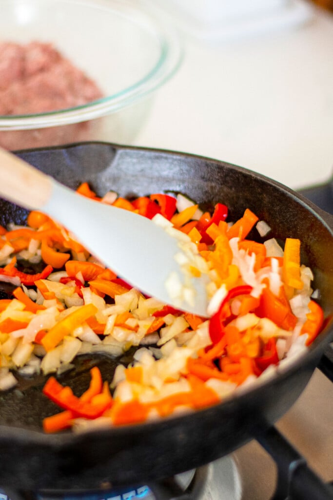 peppers and onions being cooked in a cast iron skillet on the stovetop.