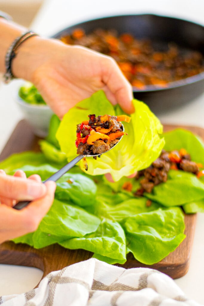 woman putting ground pork into a lettuce cup.