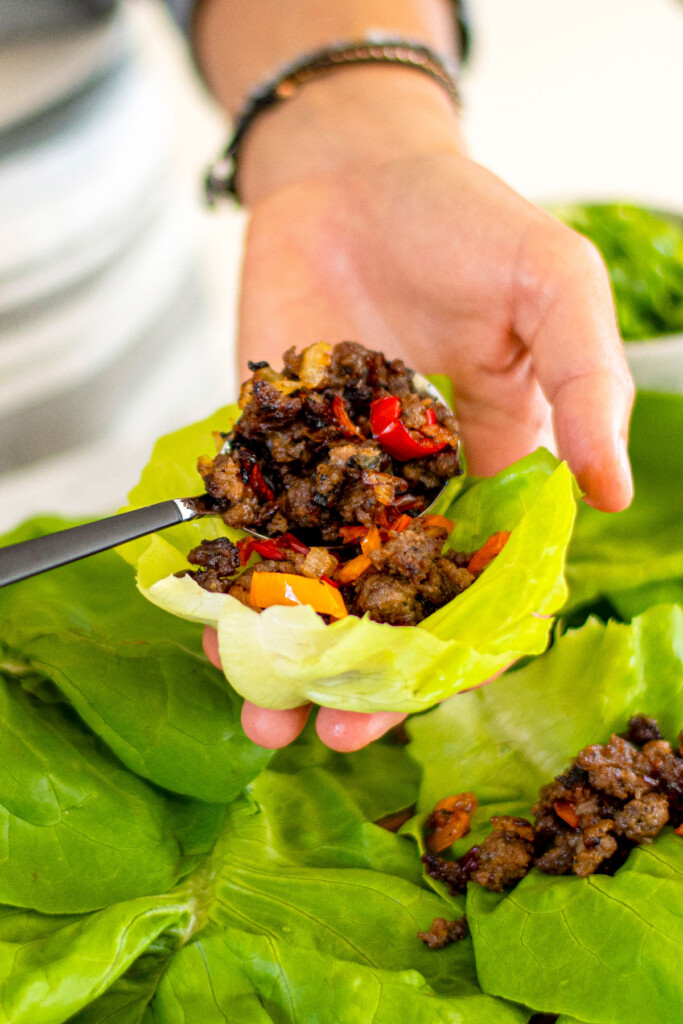 woman putting ground pork into a lettuce cup.