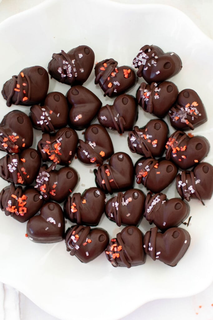 dark chocolate almond hearts with chocolate drizzle and naturally colored red and pink decorating sugars on a white plate.