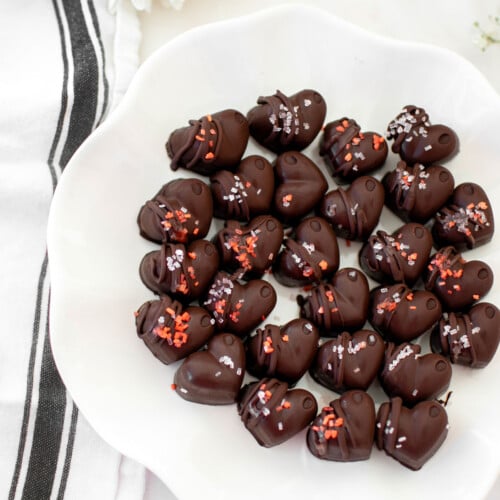 dark chocolate almond hearts on a ruffle plate on a white marble counter with fresh flowers.
