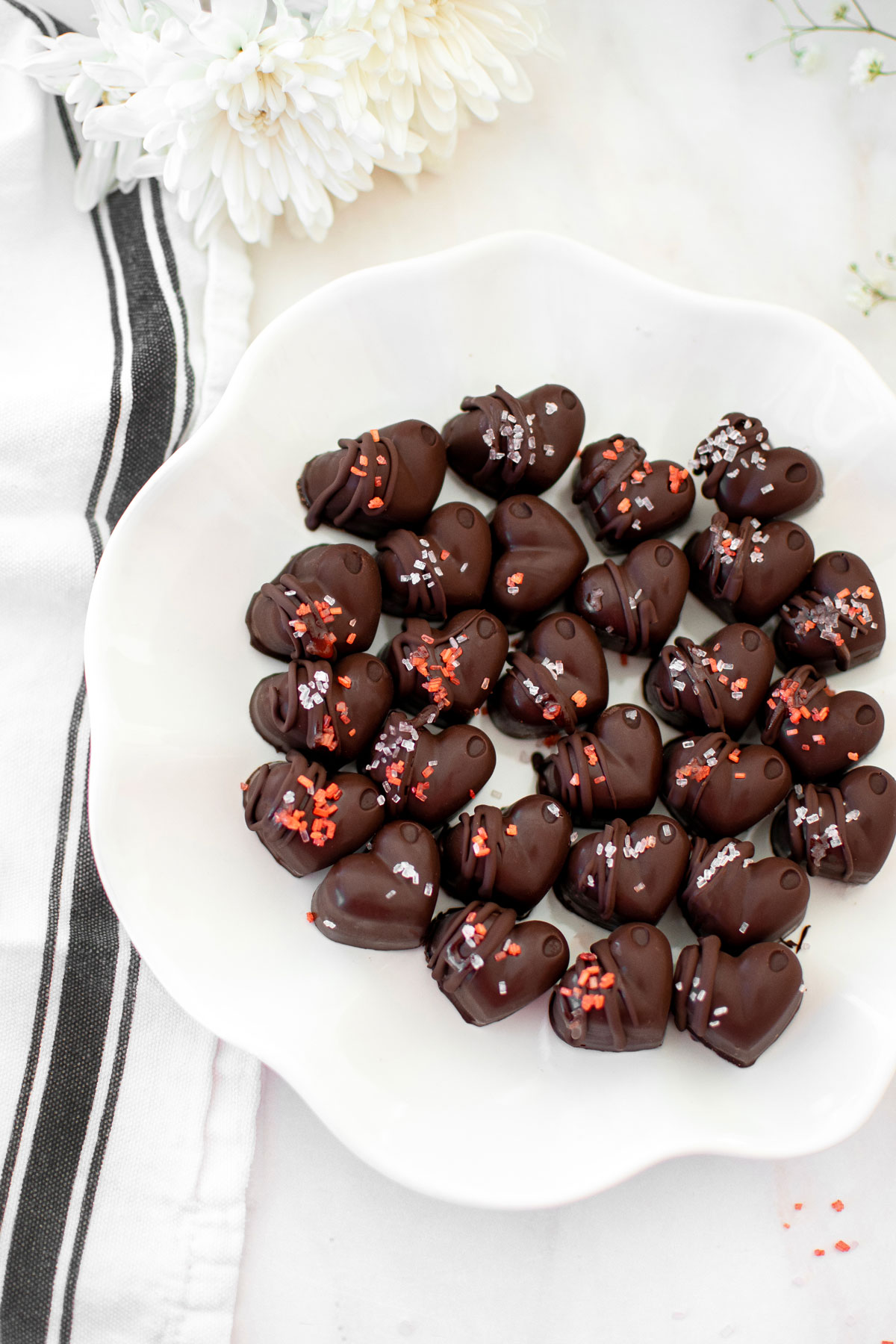 dark chocolate almond hearts on a ruffle plate on a white marble counter with fresh flowers.
