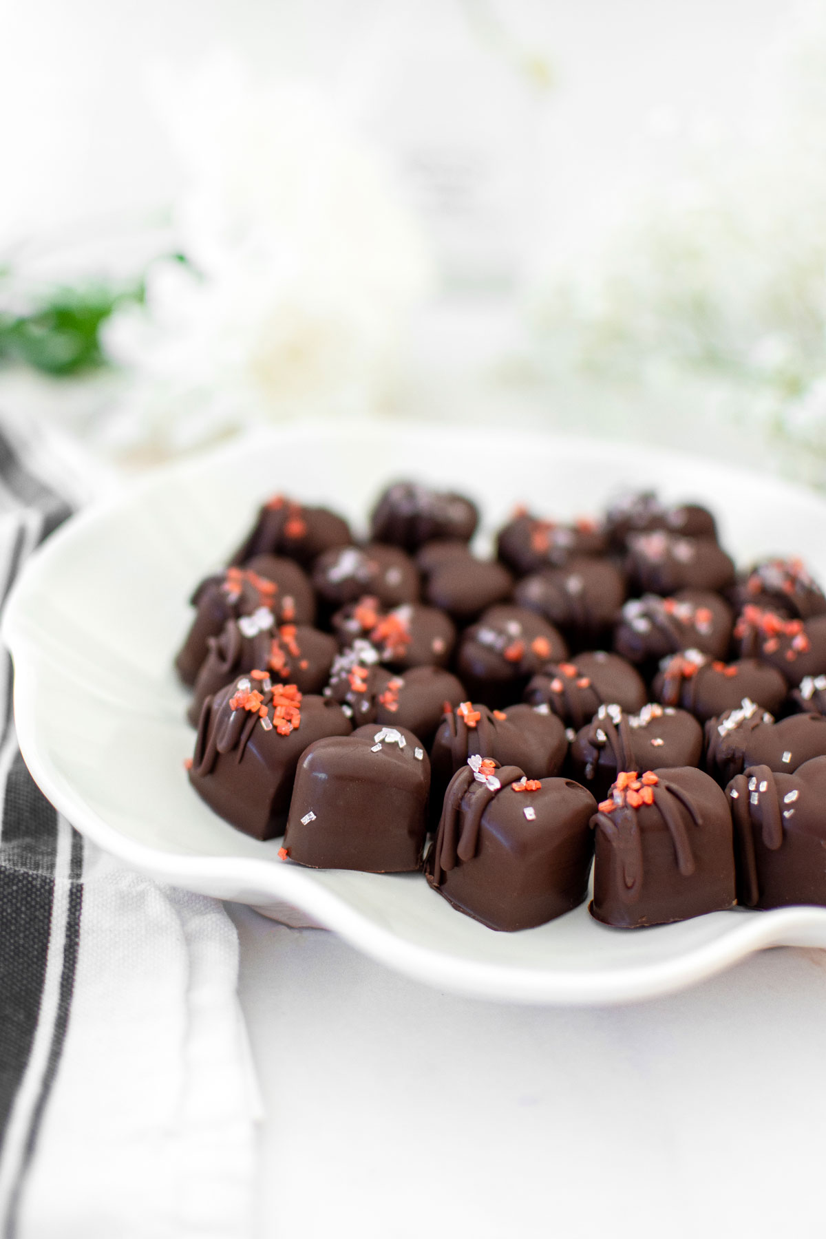 dark chocolate almond hearts on a ruffle plate on a white marble counter with fresh flowers.