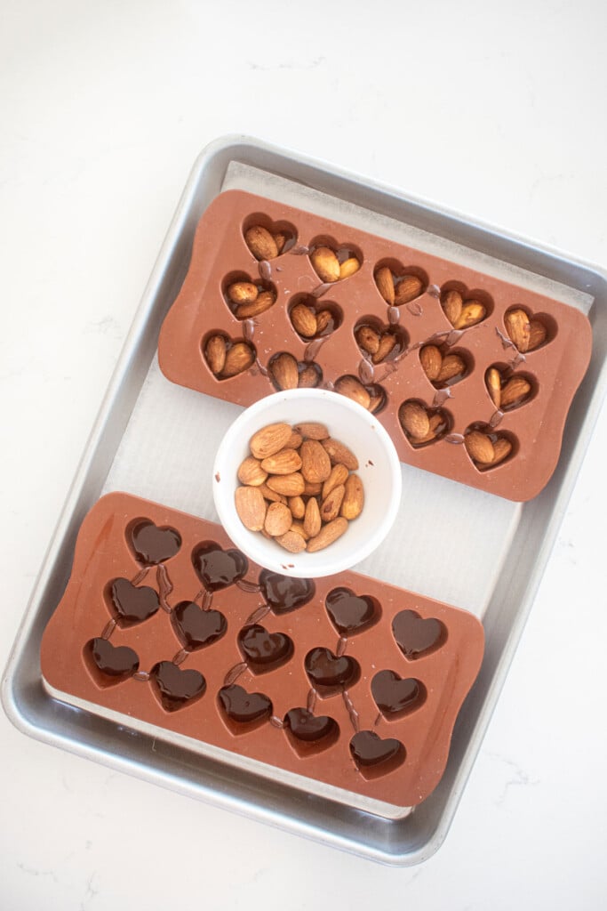 dark chocolate almond heart candies being made in candy molds on a baking sheet on a marble counter.