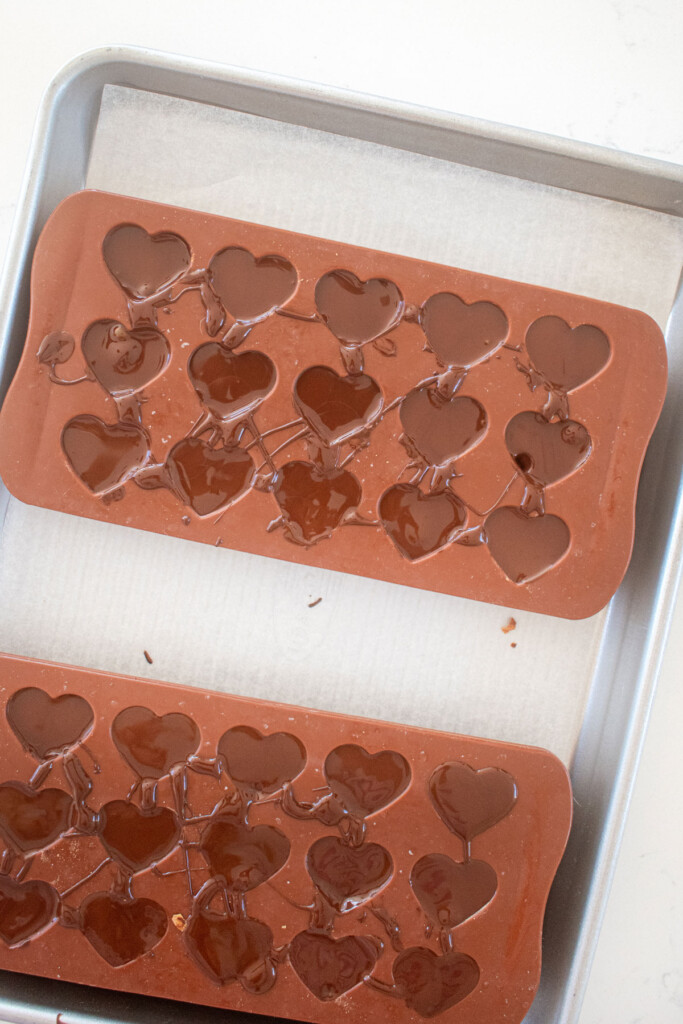 dark chocolate almond heart candies in candy molds on a baking sheet on a marble counter.