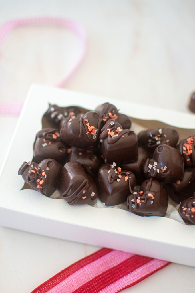 dark chocolate almond hearts in a white candy box on a marble counter with pink ribbon.