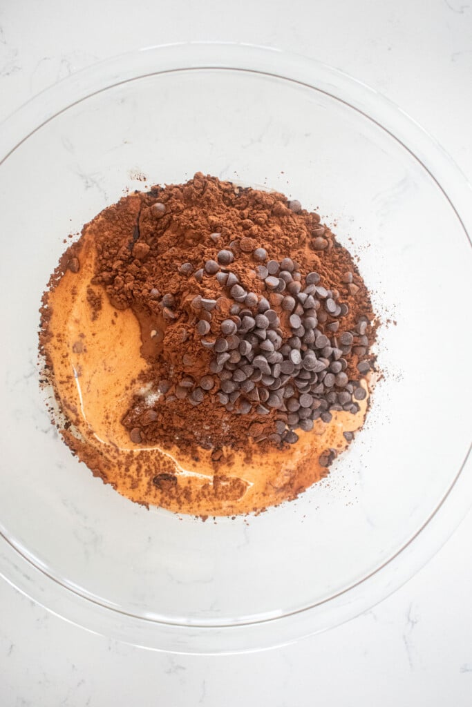ingredients for eggless chocolate ganache brownies in a glass mixing bowl on a white marble counter.