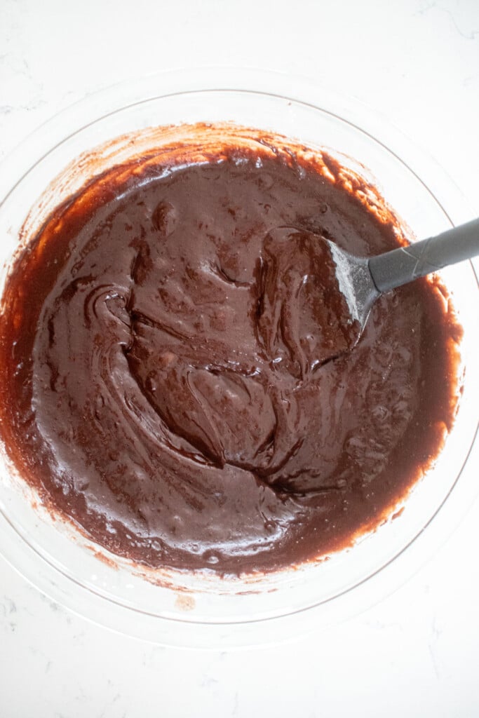 eggless chocolate ganache brownie batter in a glass mixing on a white marble counter.