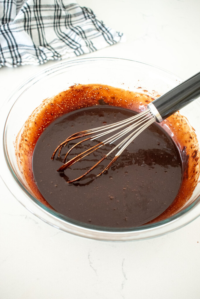 wet ingredients whisked together for eggless brownies in a large mixing bowl on a white marble counter.