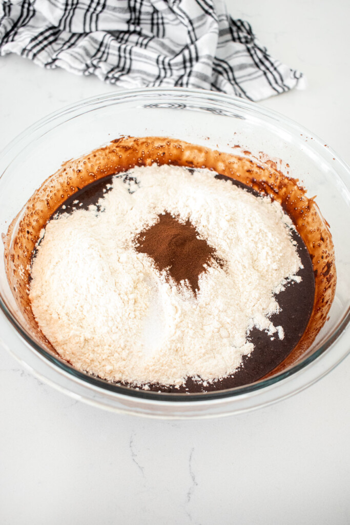dry ingredients being added to wet ingredients for eggless brownies in a glass mixing bowl on a marble counter.