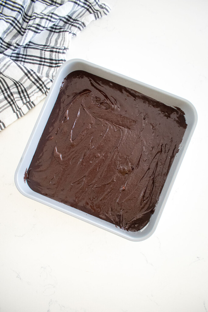 square baking pan with brownie batter spread evenly on a white marble counter.